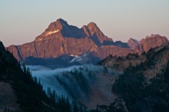 Black Peak glows pink in the early morning, with a river of fog that cascades over the foreground ridge.